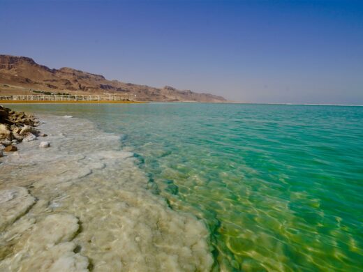 Blick auf das türkisblaue Wasser des Toten Meeres in Israel mit weißen Salzablagerungen